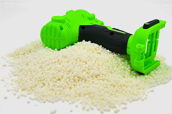 A bright green and black plastic tool handle placed on a pile of plastic resin pellets, illustrating material choice in manufacturing.