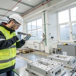 A technician in safety gear inspecting a plastic mold in a manufacturing facility.