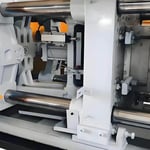 Interior view of a mechanical injection molding machine with visible cylindrical rods and operational components
