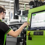 Young man interacting with a touchscreen display on a green machine in an industrial setting.