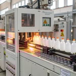 A photorealistic illustration of the blow molding process in a factory.